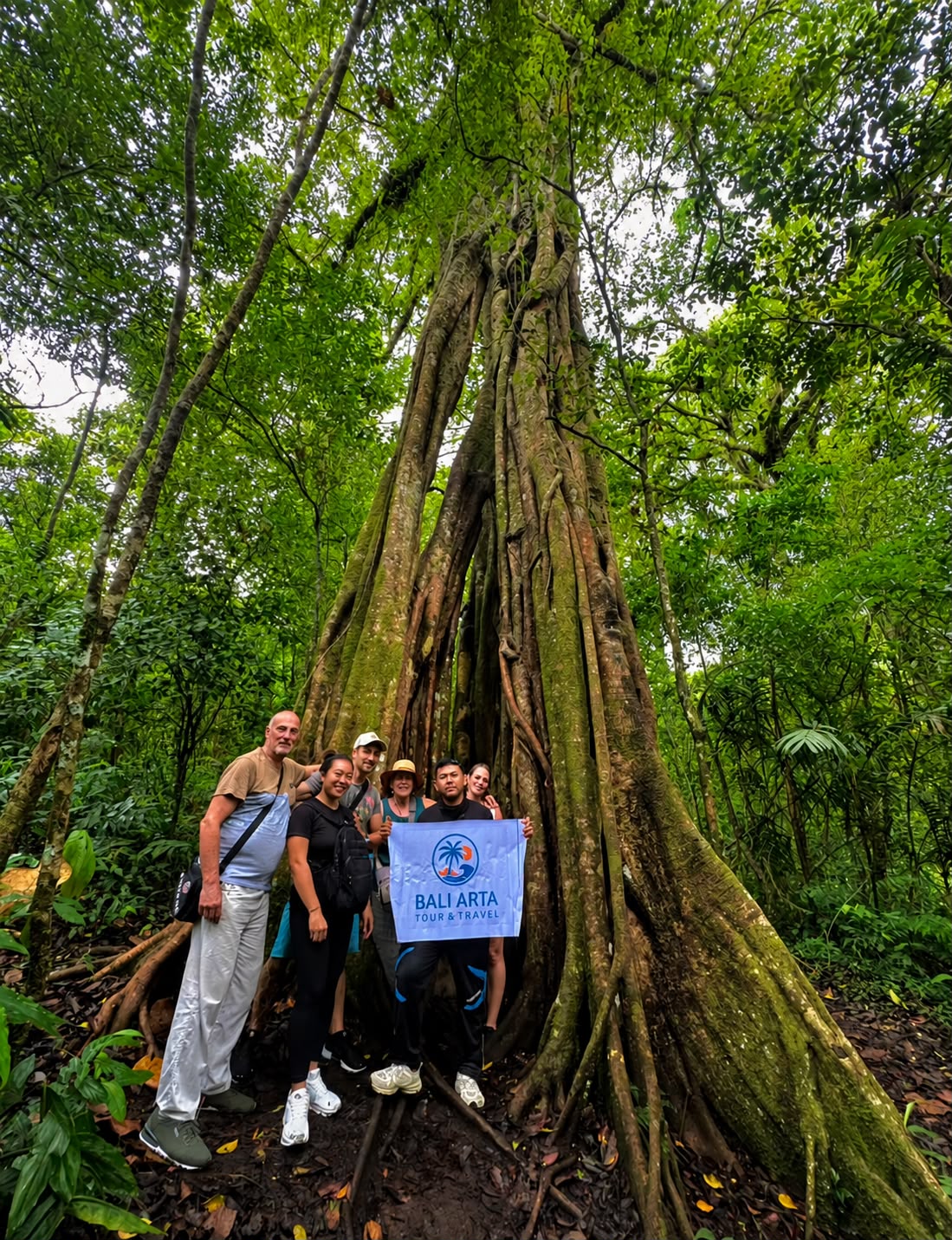 Group of travelers with Bali Arta Tour banner in front of an ancient tree